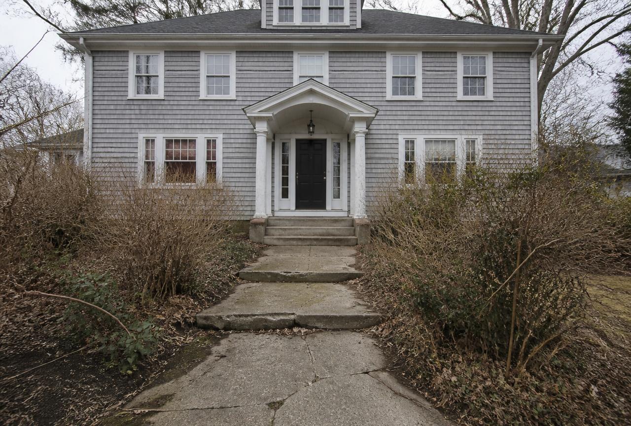 Cracked concrete front walk and overgrown shrubs at a grey shingled colonial before work