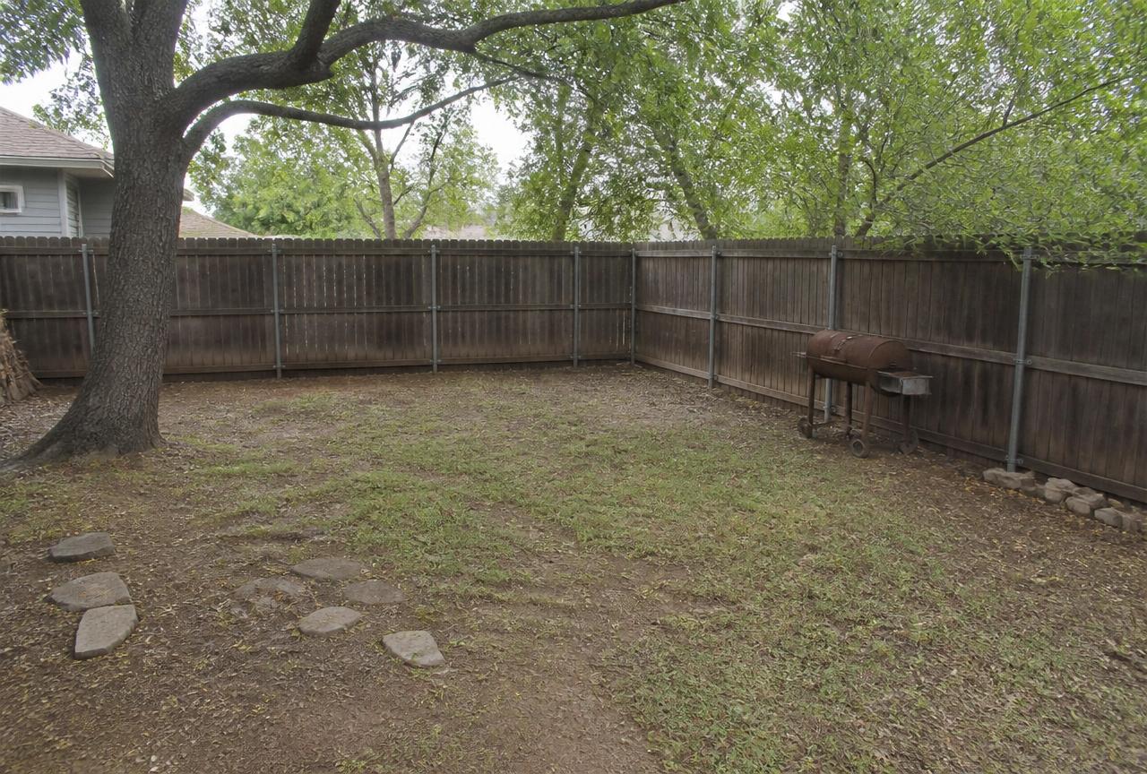 Bare worn backyard corner under a large tree with an old grill before construction